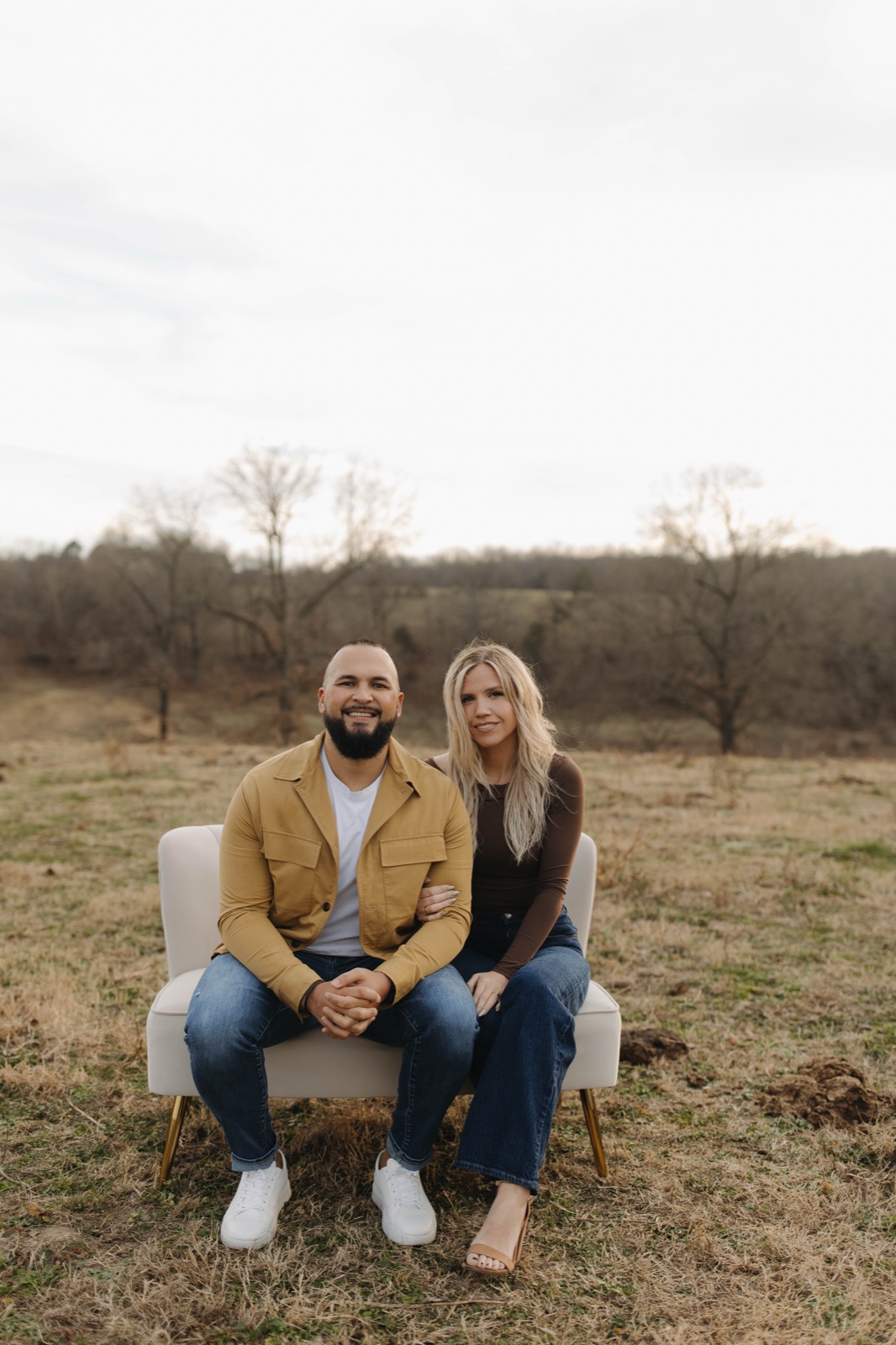 Caleb and Cortni sitting together on a loveseat in the field.