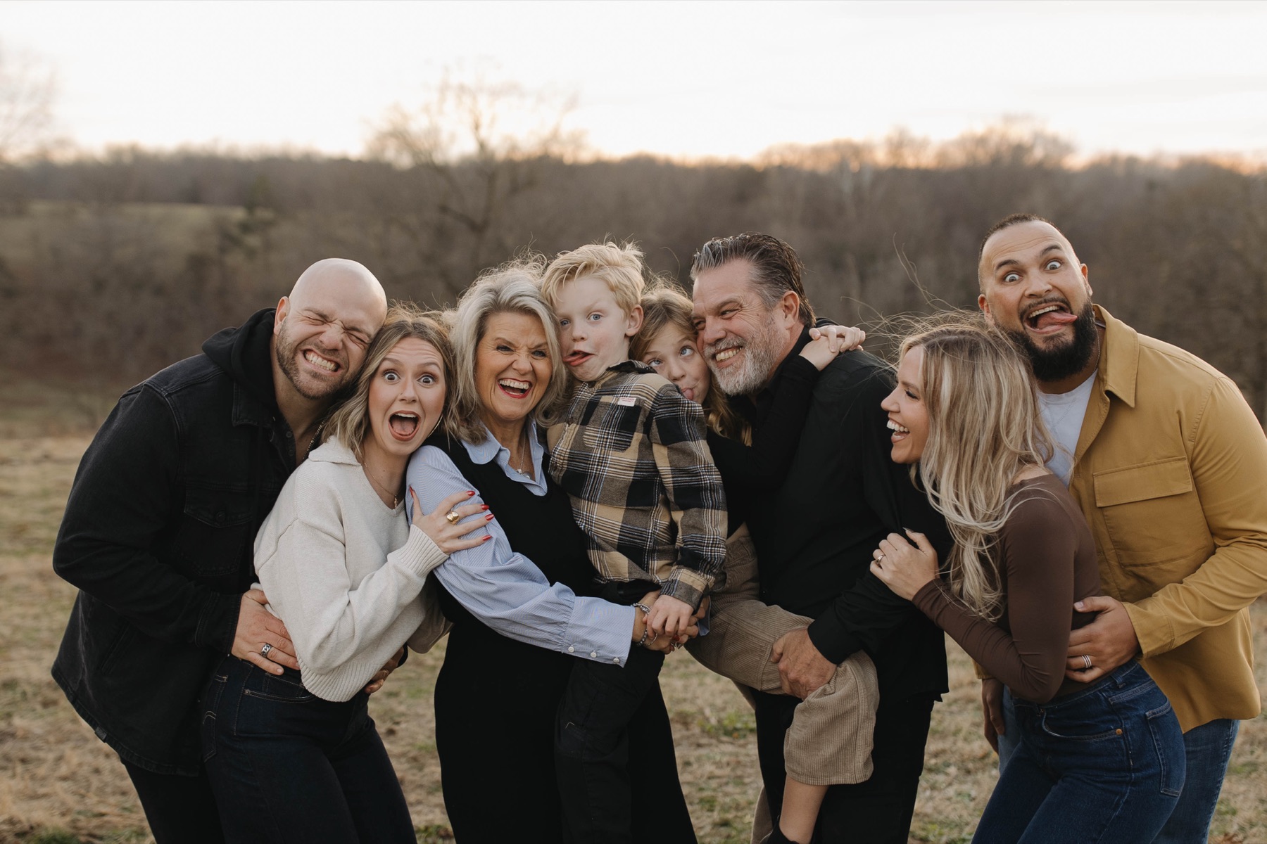 The family laughing together, making silly faces, outdoors.